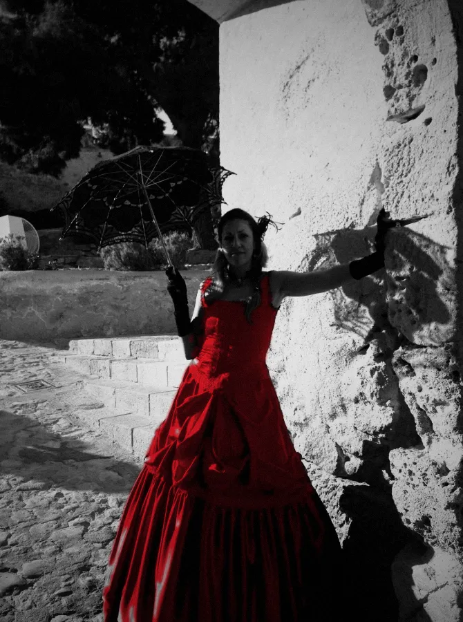 Mari Carmen Pacheco Picazo con vestido rojo y sombrilla de encaje junto a un muro de piedra